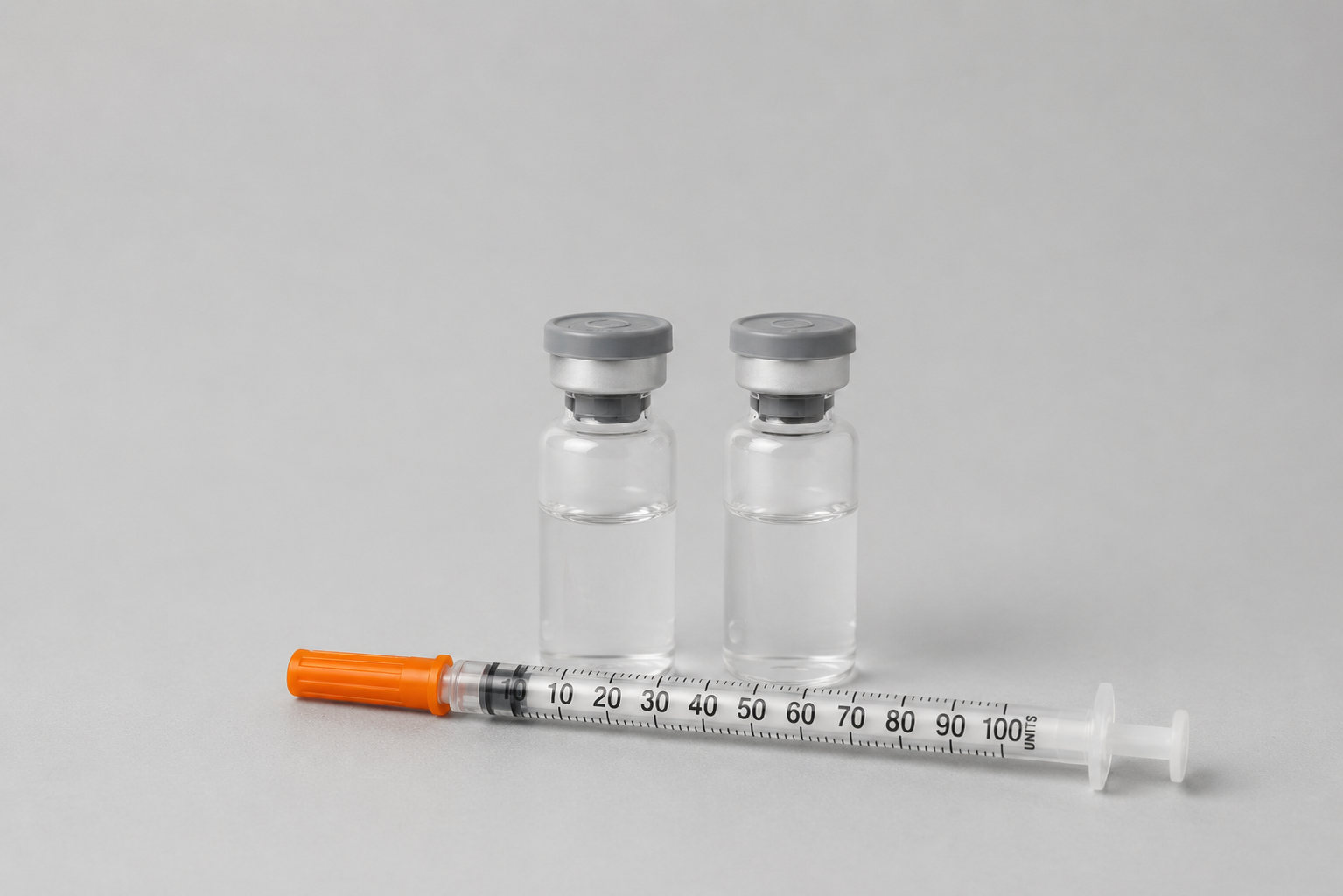 Two clear peptide vials with grey caps and a 1 mL U-100 insulin syringe with an orange plunger on a neutral background.