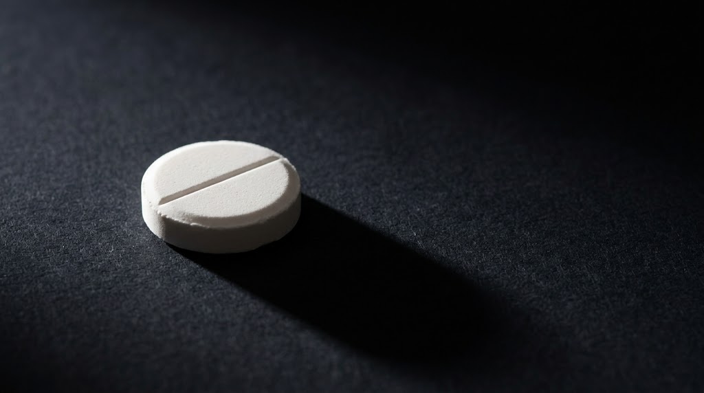 A white scored tablet casting a long shadow on a dark textured surface