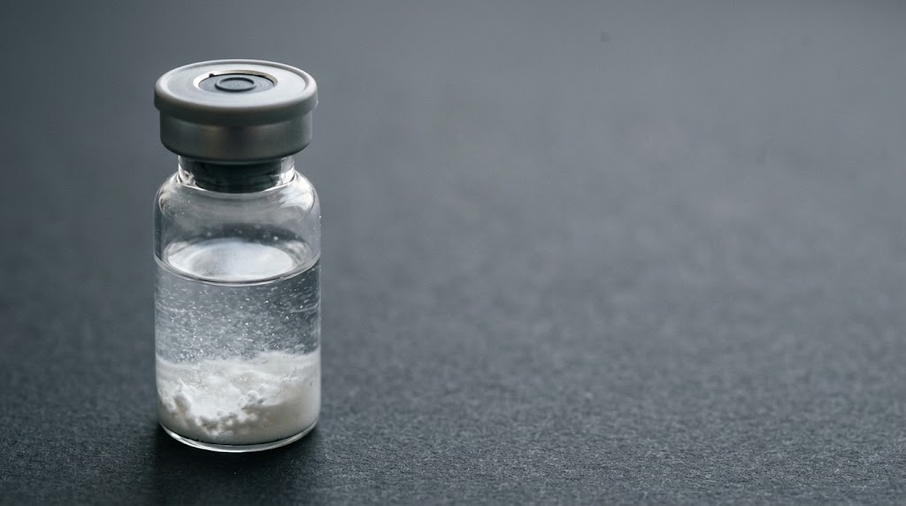 A glass vial with undissolved white peptide powder beneath clear liquid