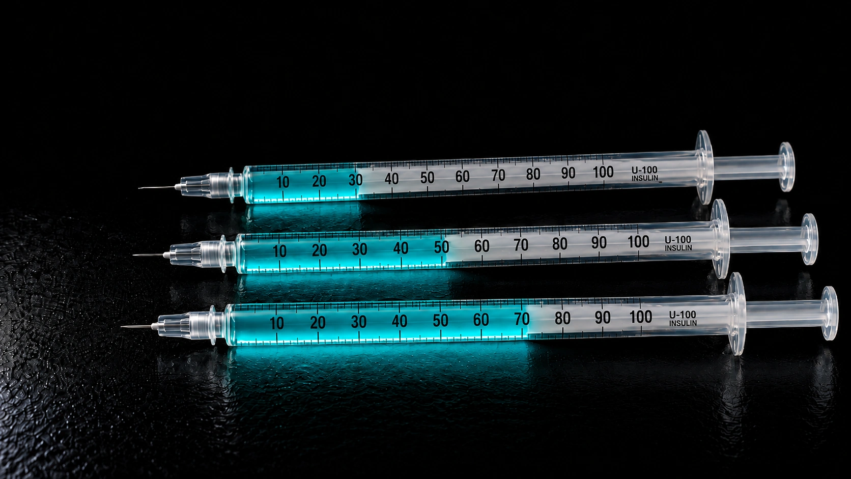 Three U-100 insulin syringes with teal liquid on a dark surface