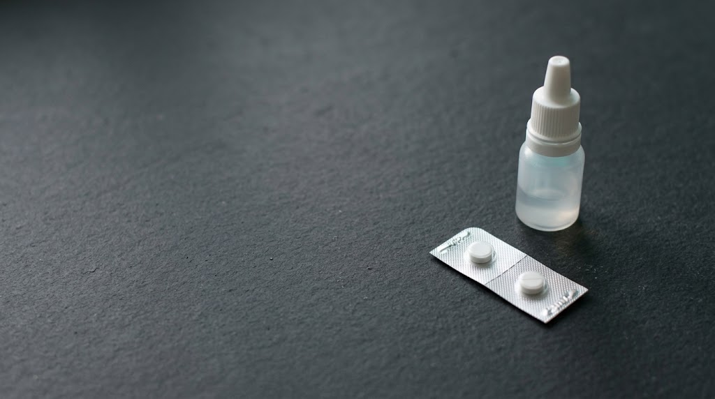 A nasal dropper bottle beside a blister pack on a dark textured surface