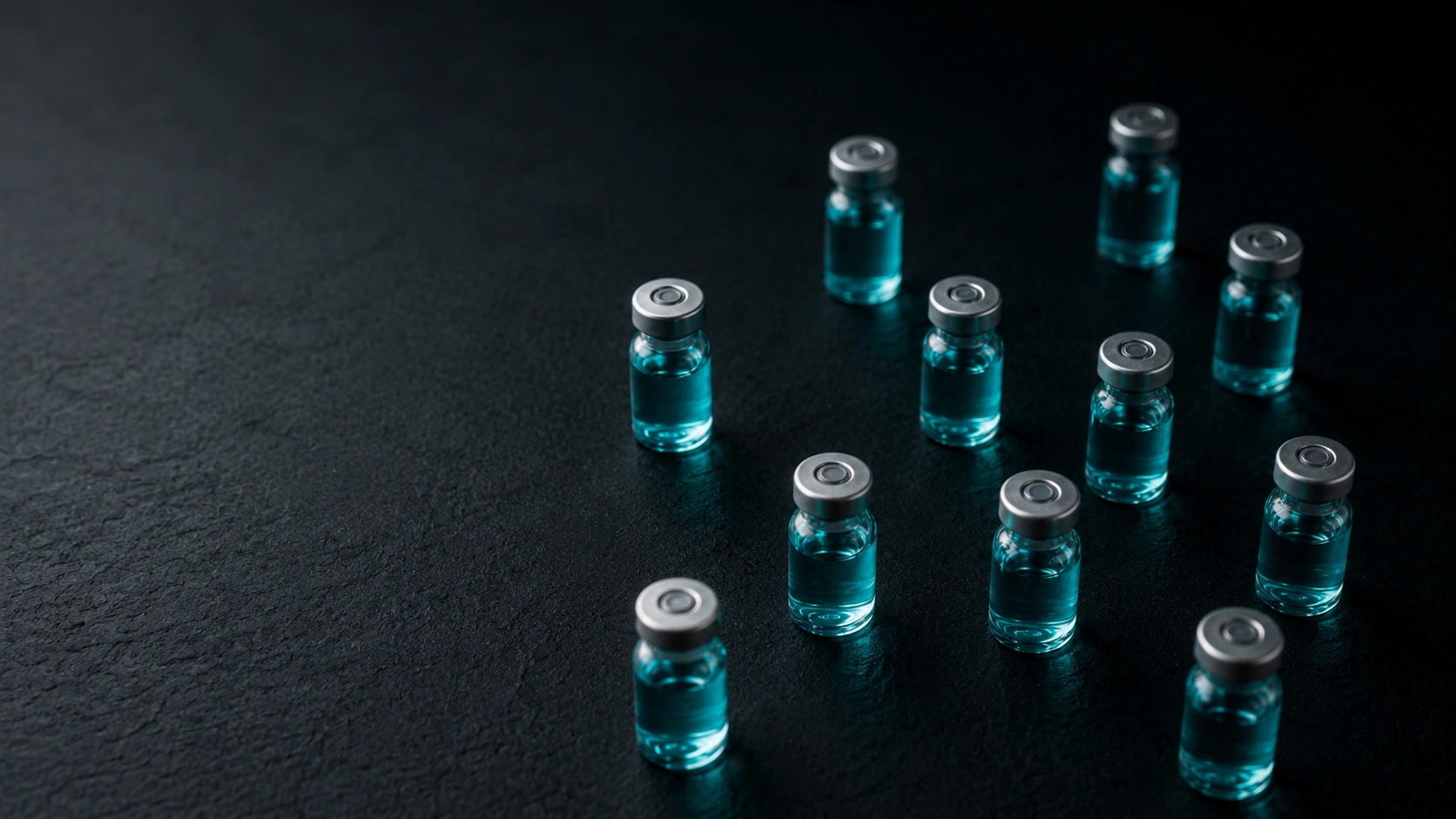 Rows of glass peptide vials with teal liquid on a dark surface